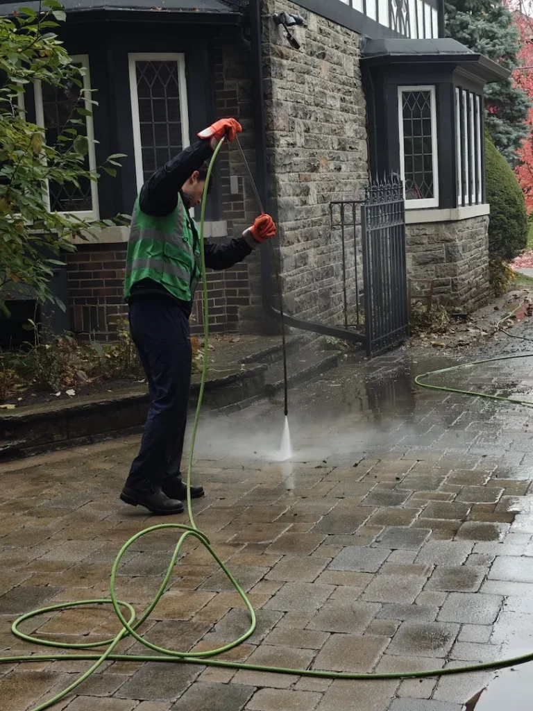 Technician pressure washing a stone driveway in front of a residential home
