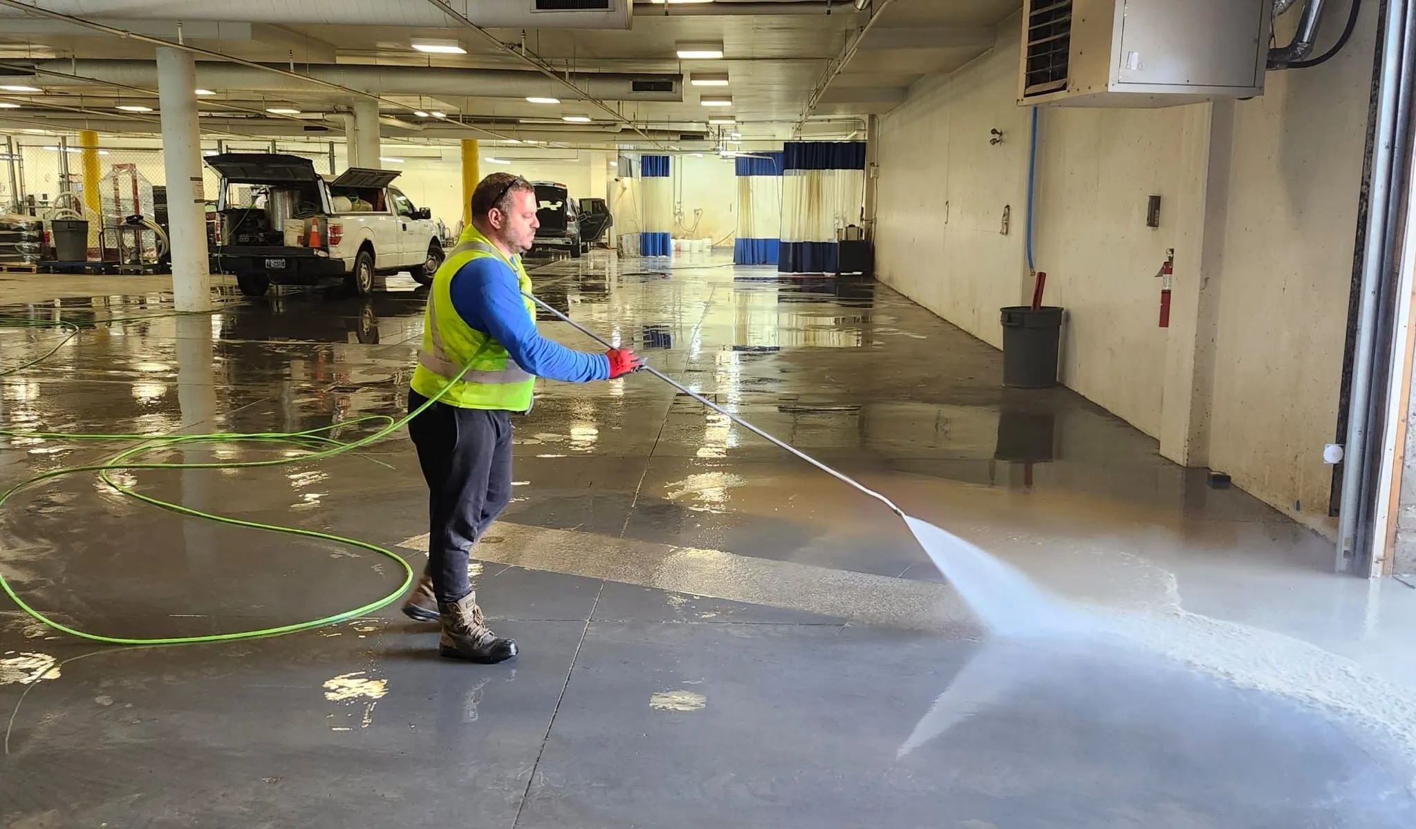 Technician pressure washing a commercial garage floor near service bays