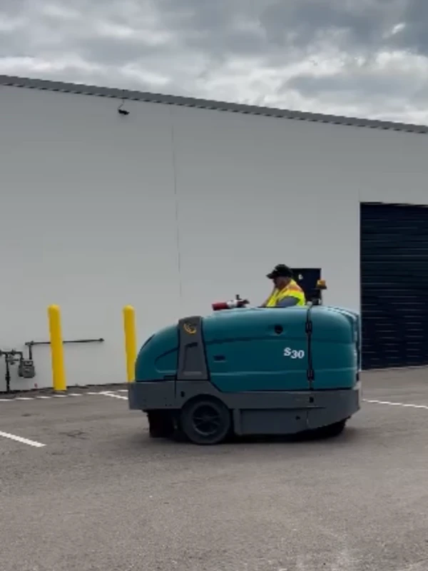 A professional operator using an S30 industrial ride-on power sweeper to clean an outdoor parking lot, demonstrating the precision and efficiency of GPM Cleaning Services.