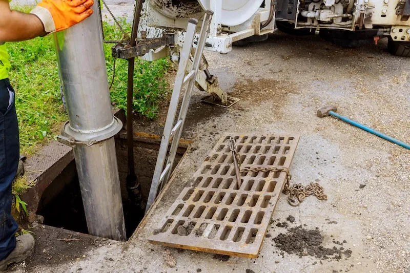 Vacuum truck cleaning a storm drain catch basin with open grate and suction hose in Etobicoke