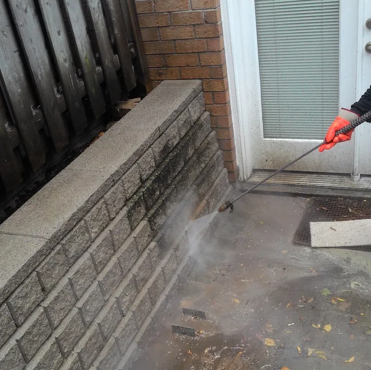Technician pressure washing stained concrete steps and retaining wall near home entrance