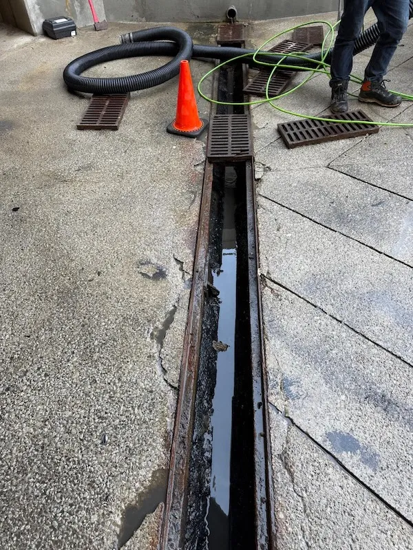 Open catch basin trench being cleaned by GPM Cleaning Services' technician using industrial vacuum and hose in Etobicoke commercial parking area