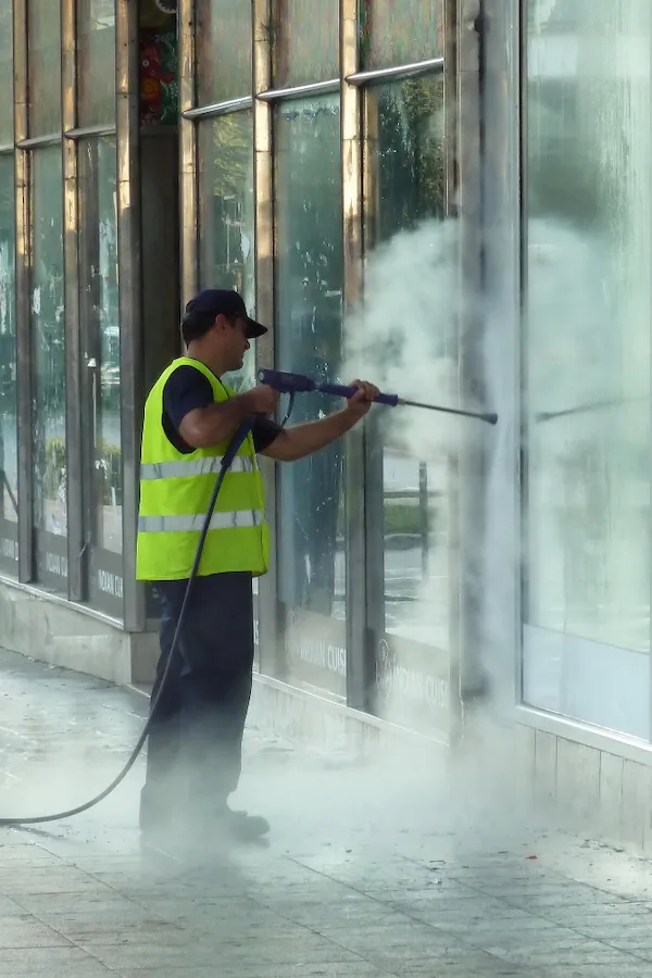 Worker is pressure washing a storefront window to remove dirt and grime
